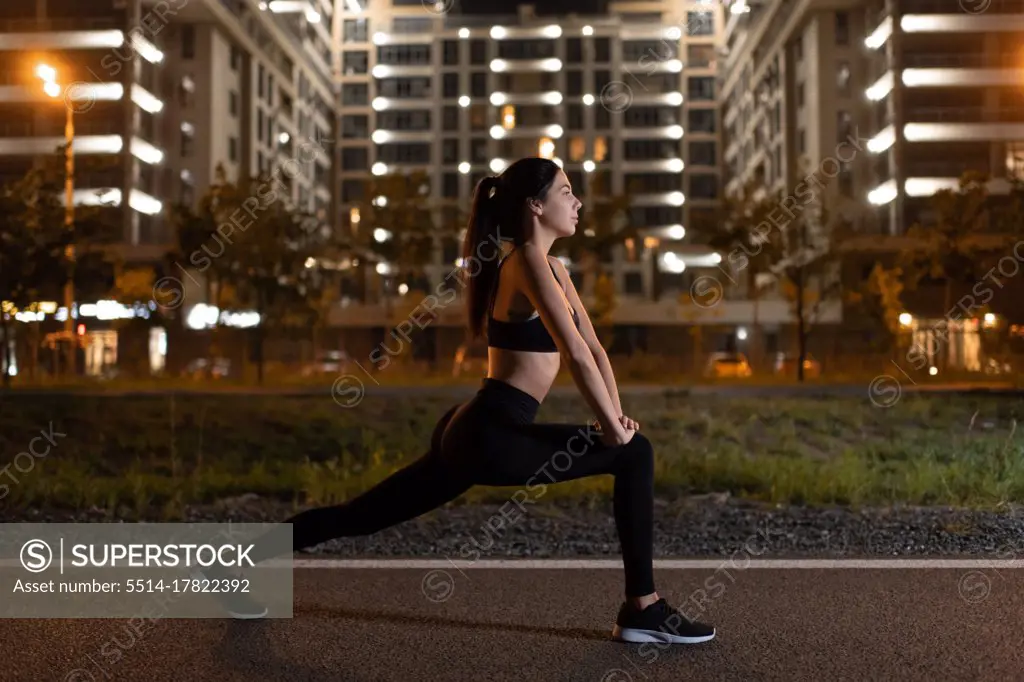 Fit sportswoman stretching legs during night workout