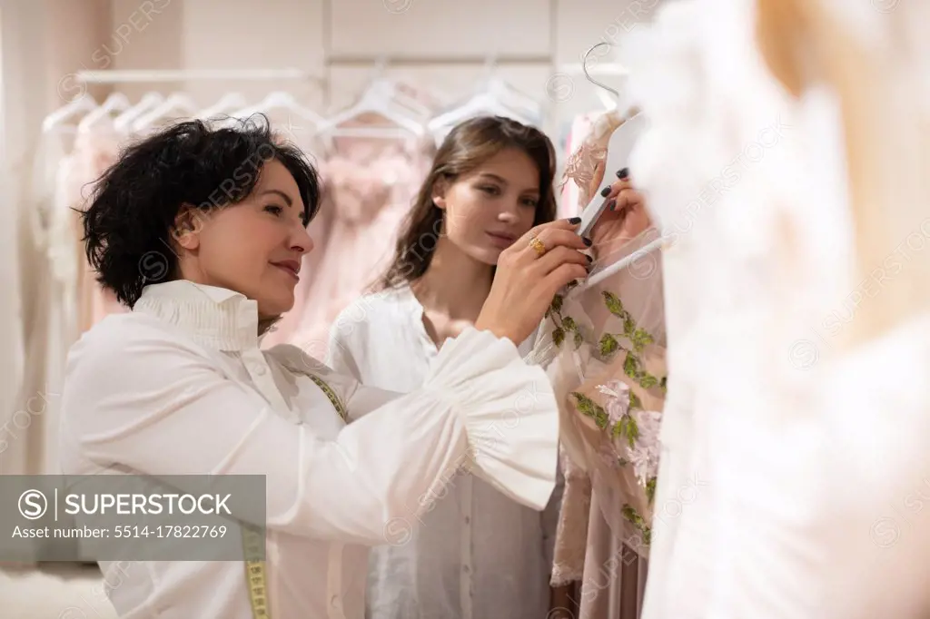 Female boutique owner assisting young woman and presenting dresses