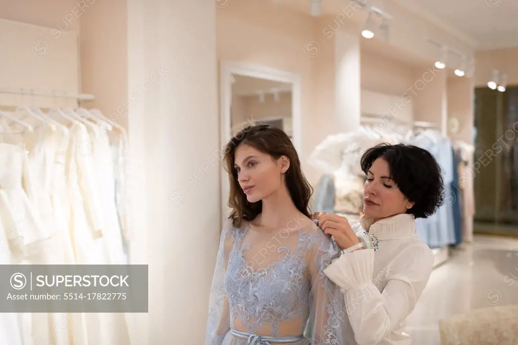 Young woman trying on dress with assistance of atelier owner