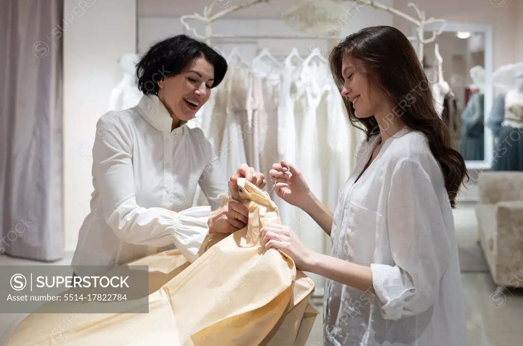 Cheerful shop owner packing dress and talking to satisfied female client