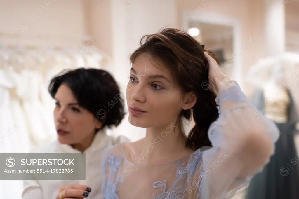 Young woman with wedding designer trying on gown and discussing hairstyle