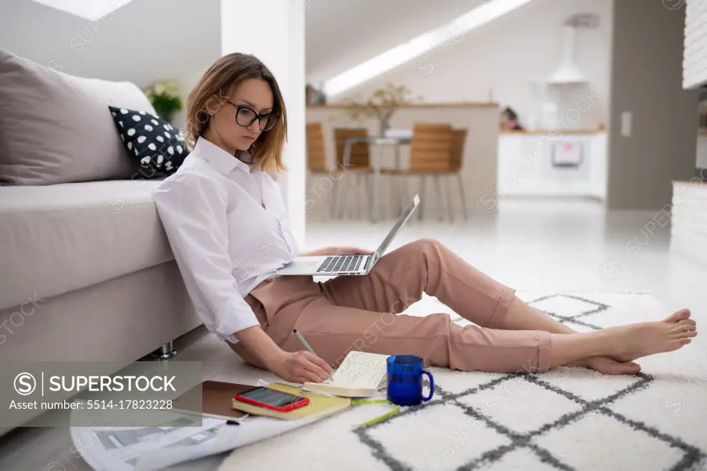 Young busy woman working with laptop and papers at home