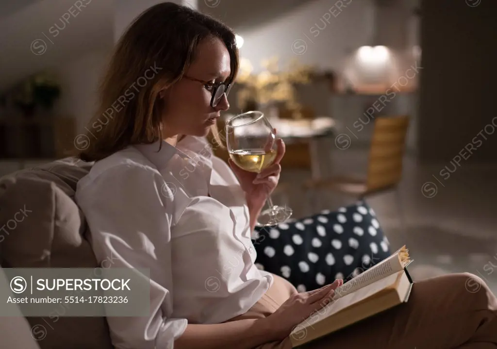 Relaxed woman enjoying wine and book at home