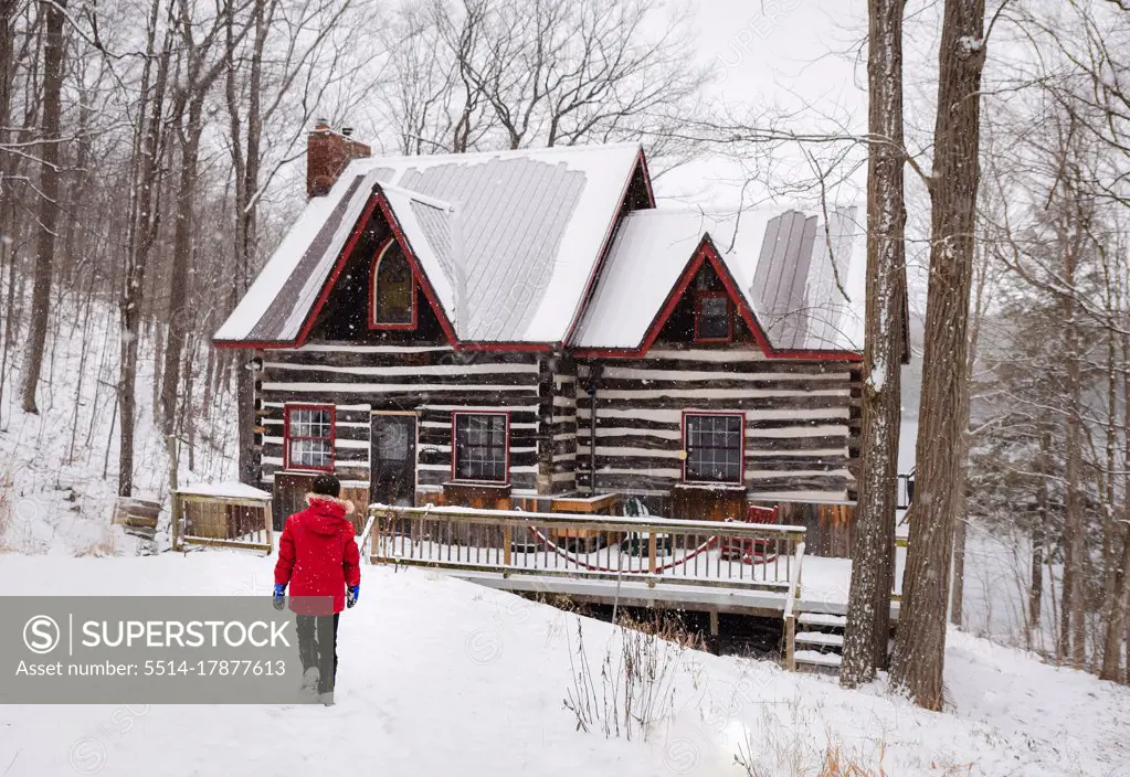Boy in red winter coat walking towards log cabin on snowy winter day.