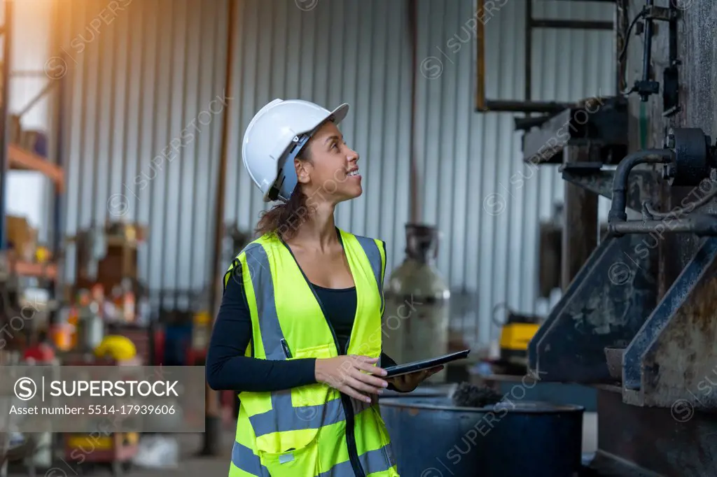 Young female in protective uniform inspecting industrial machine