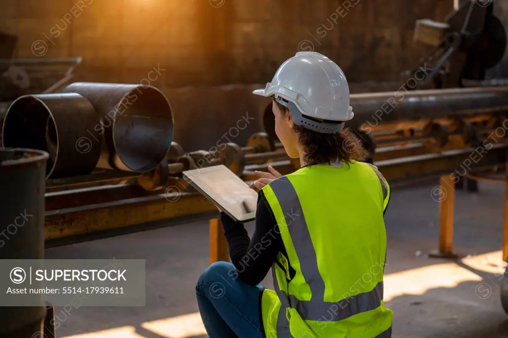 Young female in protective uniform inspecting industrial machine