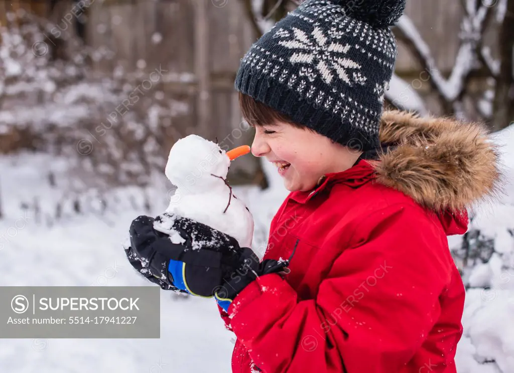Boy holding a small snowman in his hands outdoors on a snowy day.