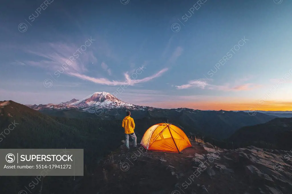 A man is standing by a tent on the top of a mountain near mt. Rainier