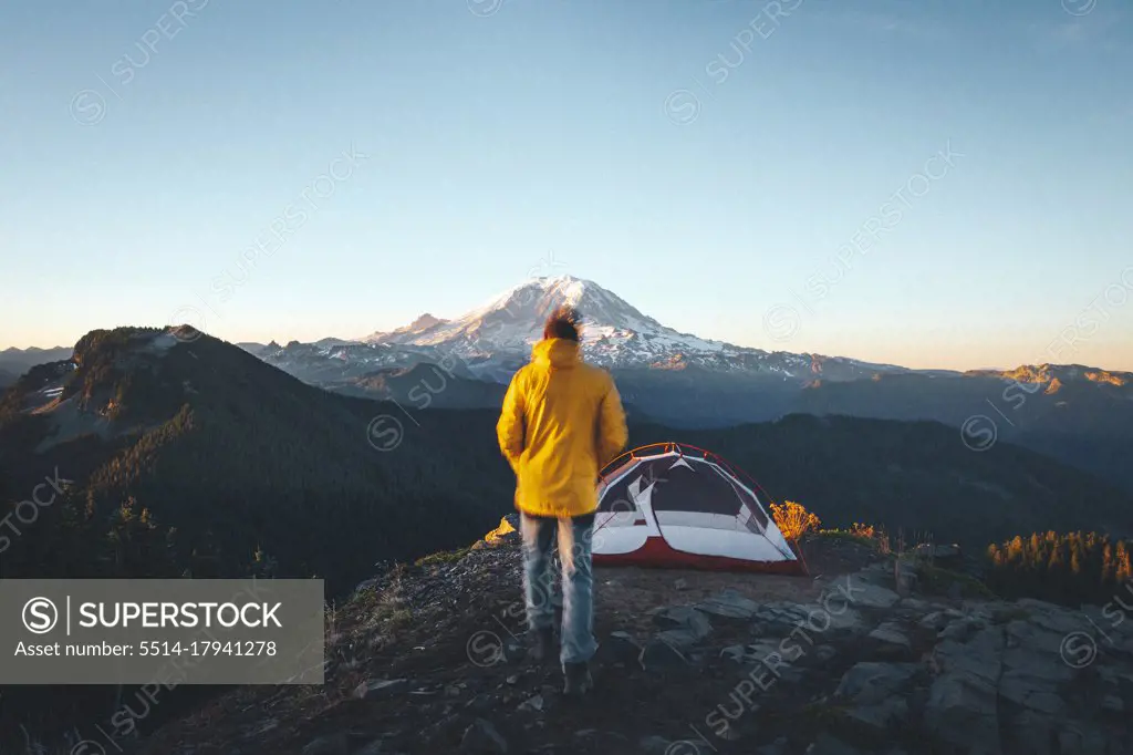 A man is walking to a tent on the top of a mountain near mt. Rainier