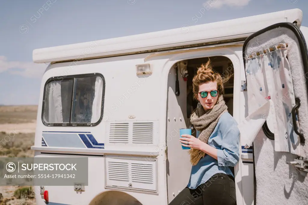 A stylish young woman drinks coffee outside of her trailer in the sun