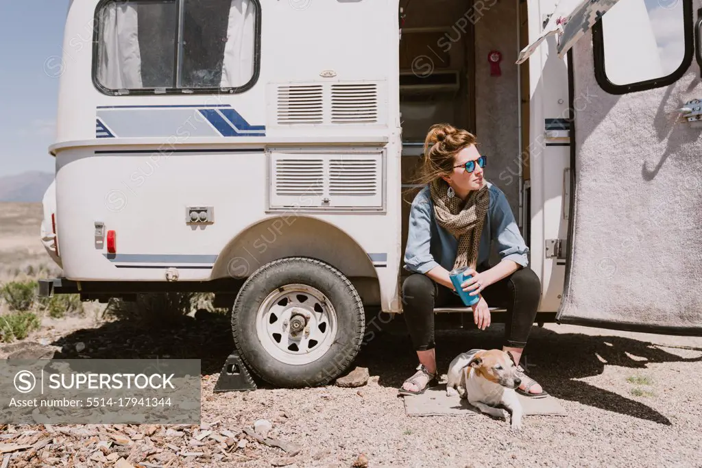 A stylish young woman and her dog sit outside their car trailer