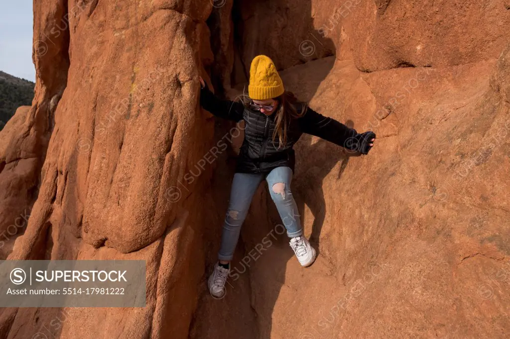 Preteen girl climbing on a rock formation on a sunny day