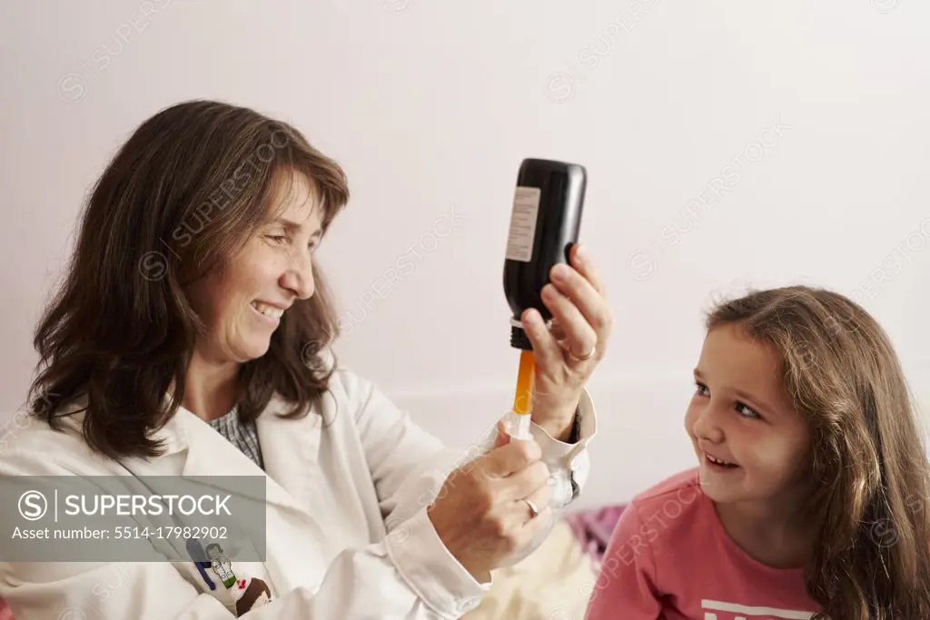 Female doctor giving syrup with syringe to a little girl at home. Home doctor concept