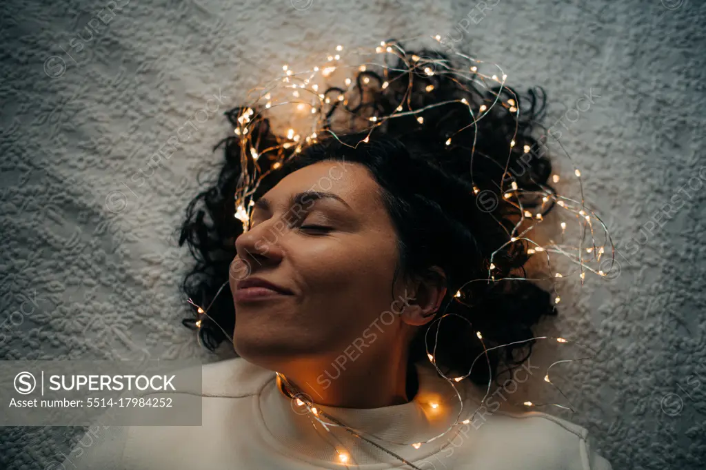 Woman lying down with tangled string lights in her hair, smiling