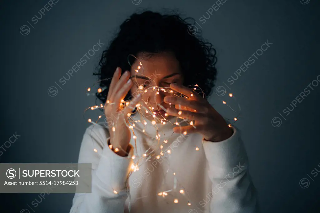 woman with curly hair holding string lights on dark background