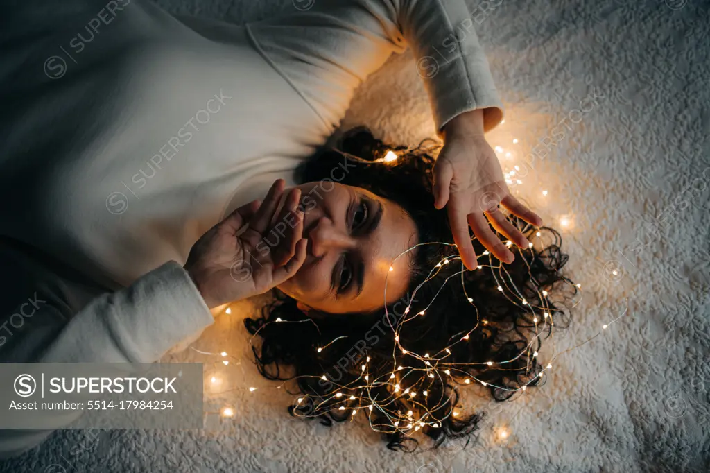Woman lying down with tangled string lights in her hair smiling