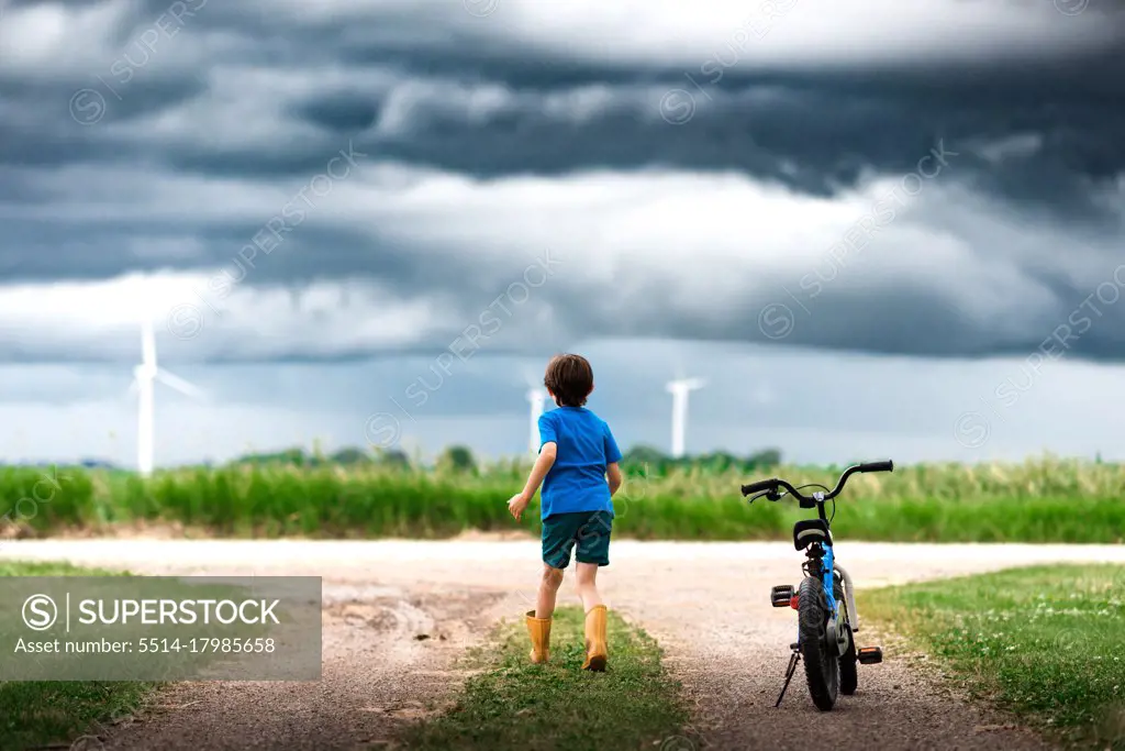 boy with bicycle watching storm clouds over a wind farm in Iowa