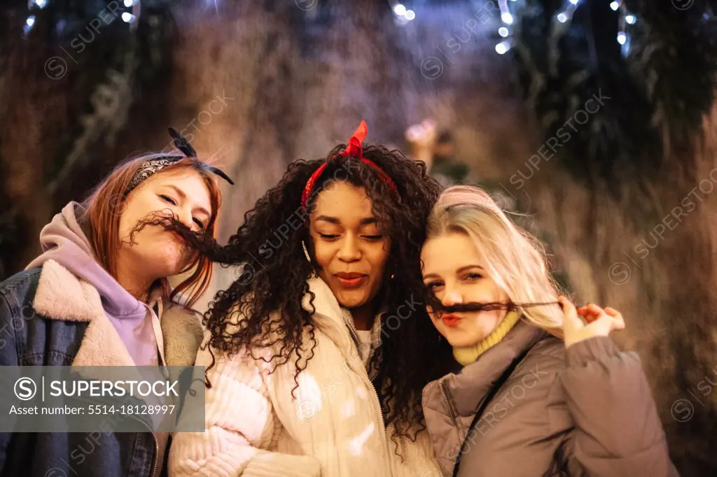 Young women making fake mustaches with their girlfriendâ€™s hair in city