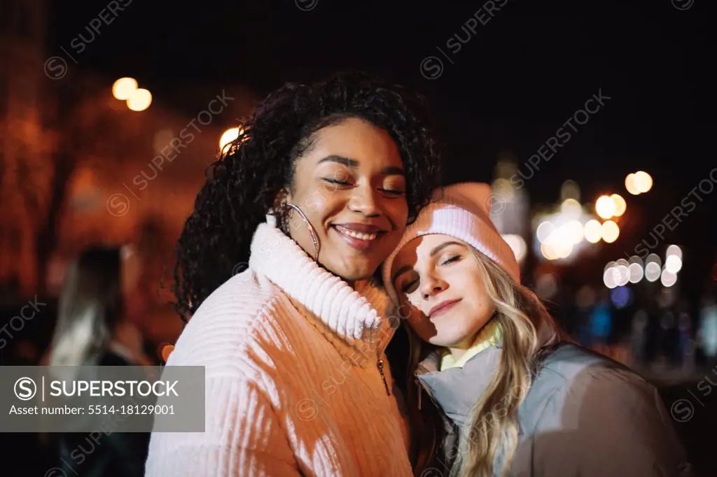 Portrait of happy girlfriends standing in city at night