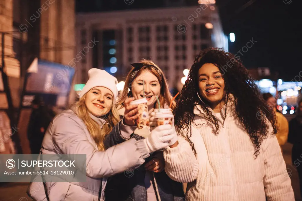 Happy female friends toasting hot drinks in city during winter