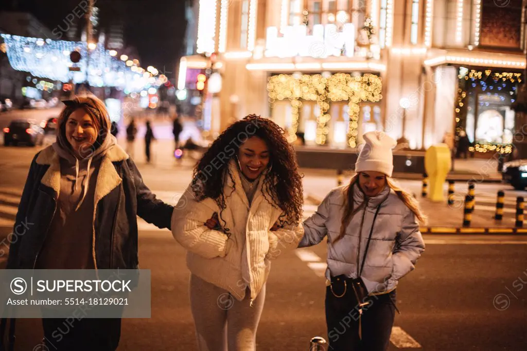 Happy female friends crossing road in city at night