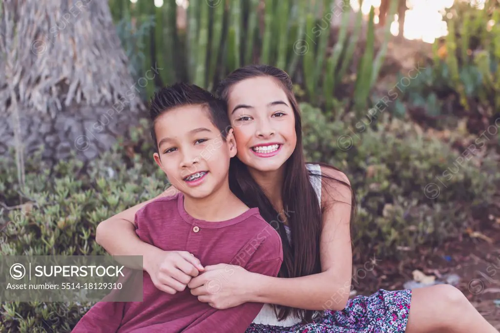 Older sister hugging young brother by a cactus garden