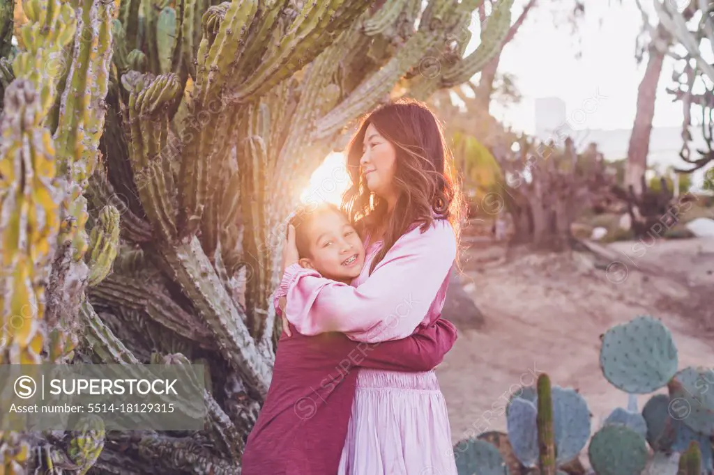Mother hugging son in front of a big cactus with back light sun.