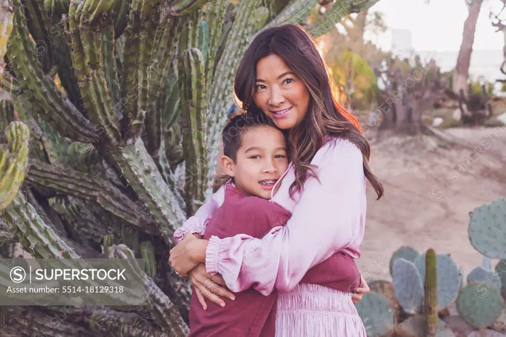 Mother hugging son in front of a big cactus, both looking at camera.
