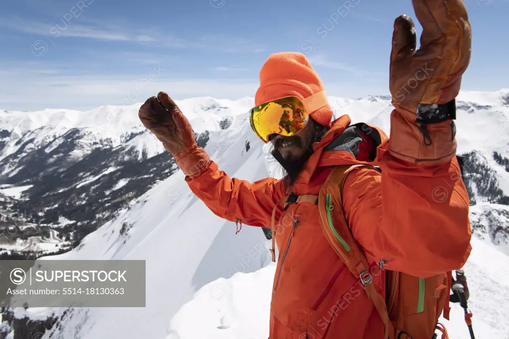 Man in warm clothing standing with arms raised on snowcapped mountain