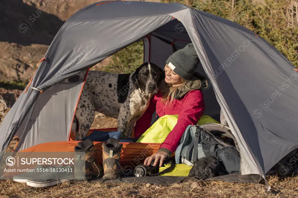 Smiling young woman with dog in tent on mountain during vacation