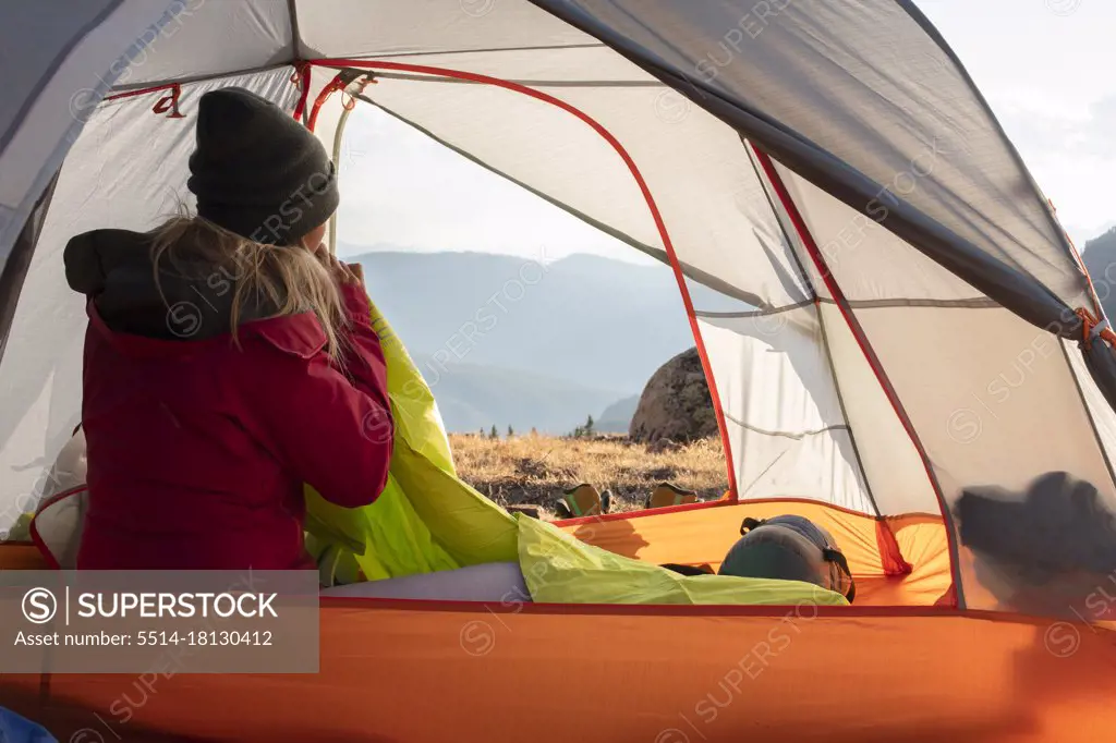 Rear view of woman blowing mattress while sitting in tent on mountain during vacation
