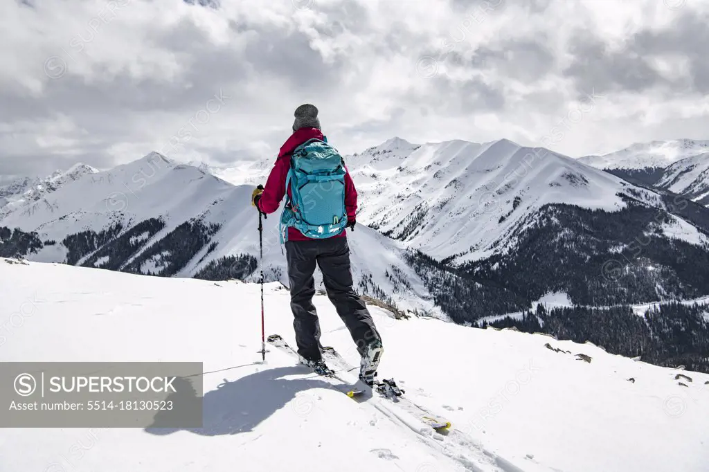 Rear view of woman with skis on snowcapped mountain against sky during vacation