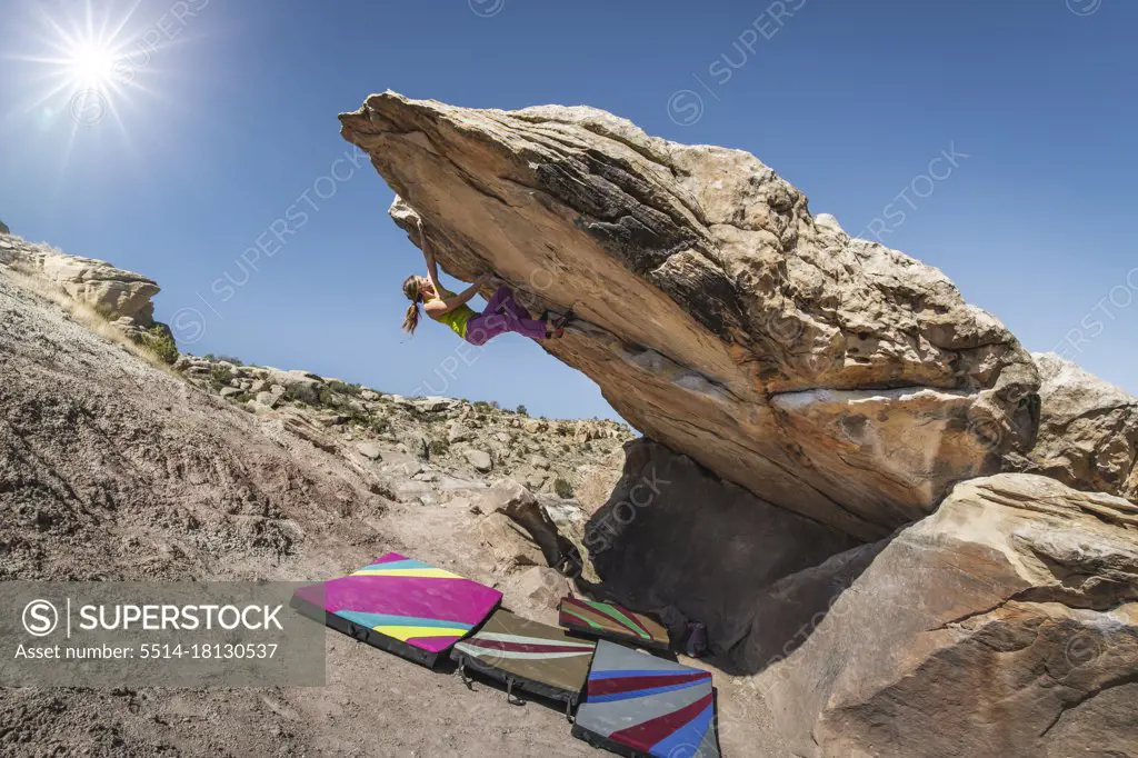 Woman practicing bouldering on rock against clear sky during sunny day