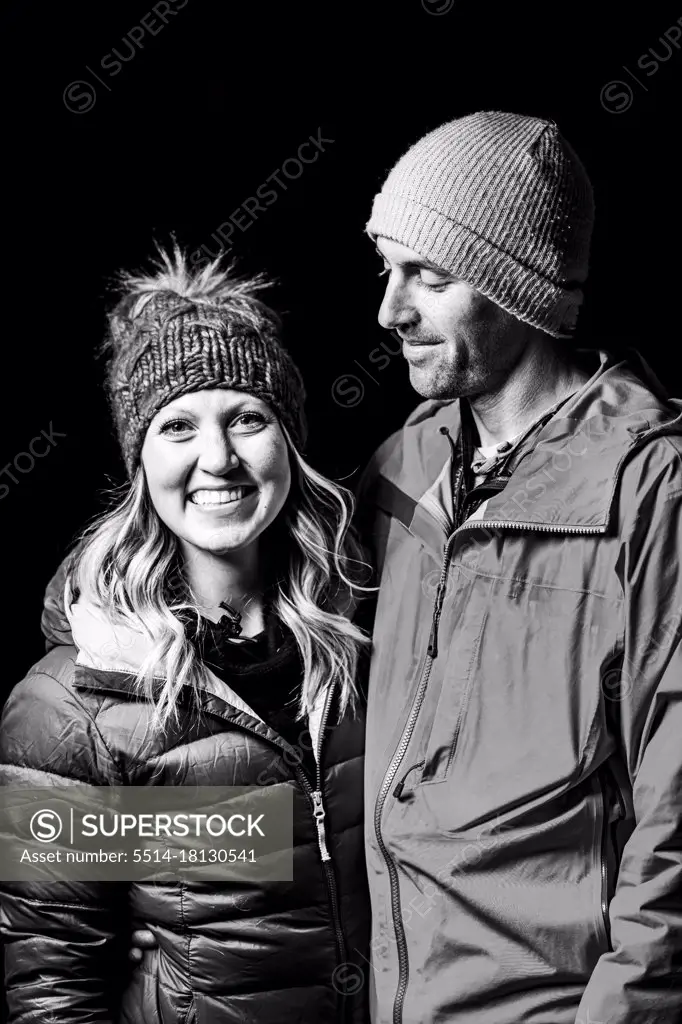 Smiling couple in warm clothing standing against black background