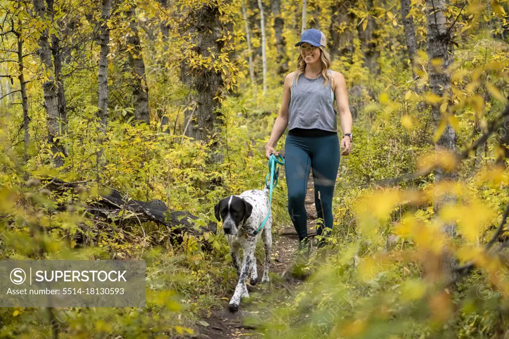 Smiling young woman walking with dog amidst autumn plants in forest