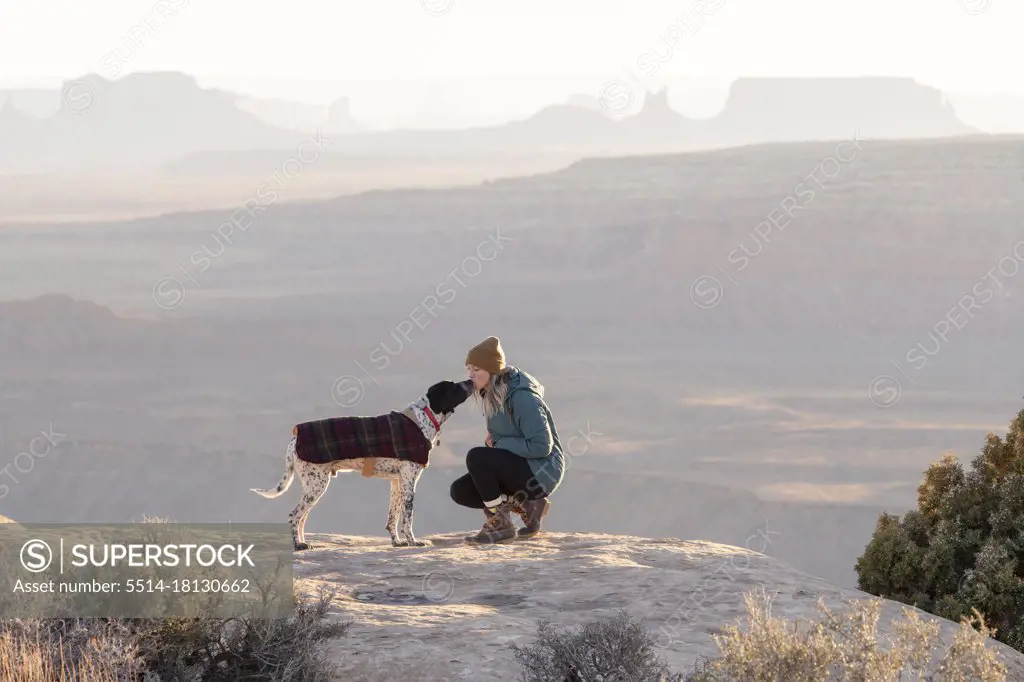 Young woman kissing dog on mountain peak at desert during vacation