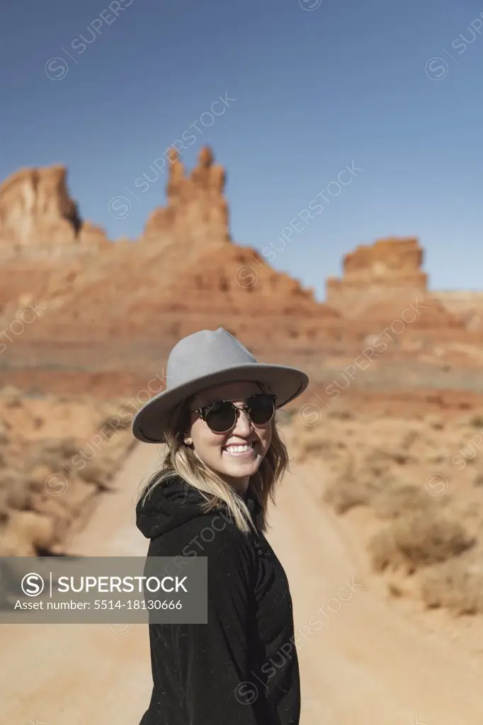 Portrait of smiling young woman in sunglasses standing on dirt road at desert