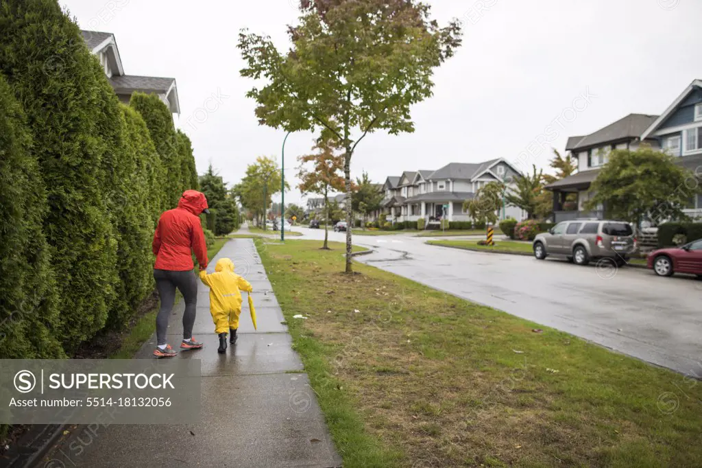 Mother walks with son on sidewalk during a rainy day.