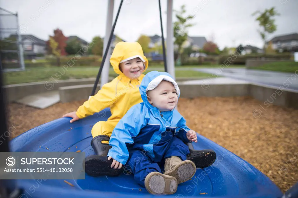 Two kids sit on a large blue swing at the park
