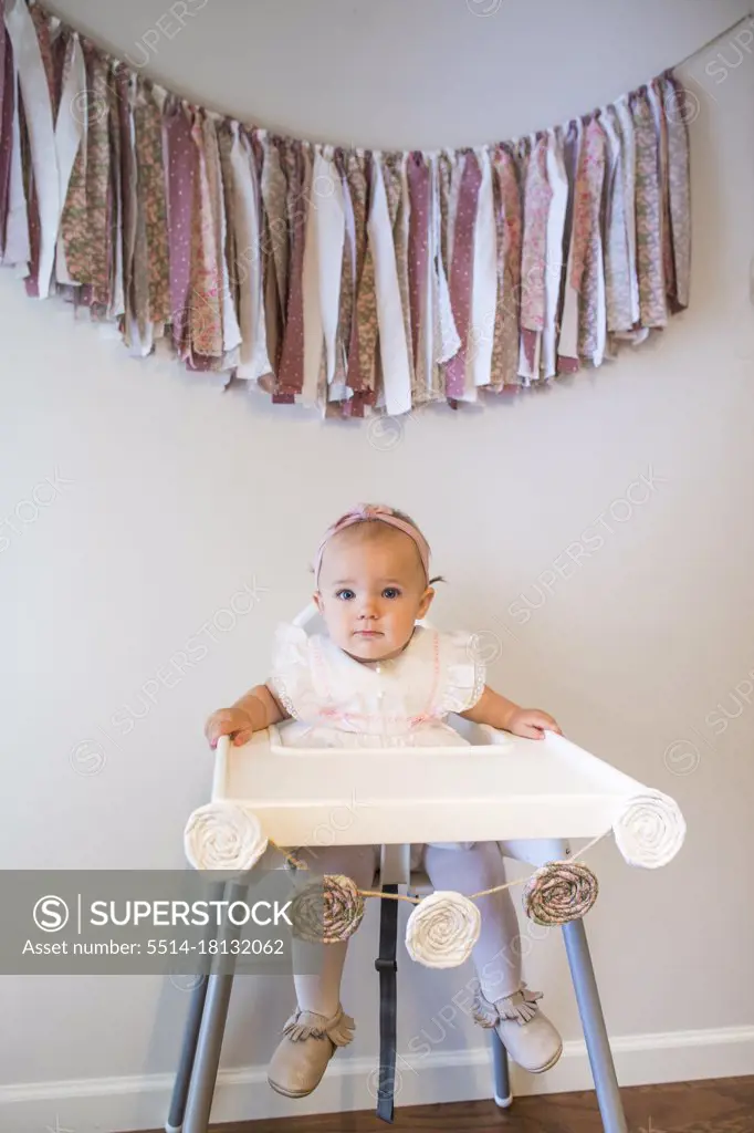 Portrait of cute one year old sitting below her birthday banner.