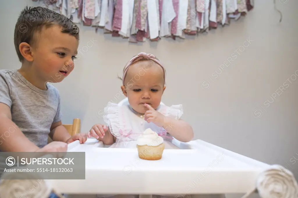 Brother helps his one year old sister on her first birthday