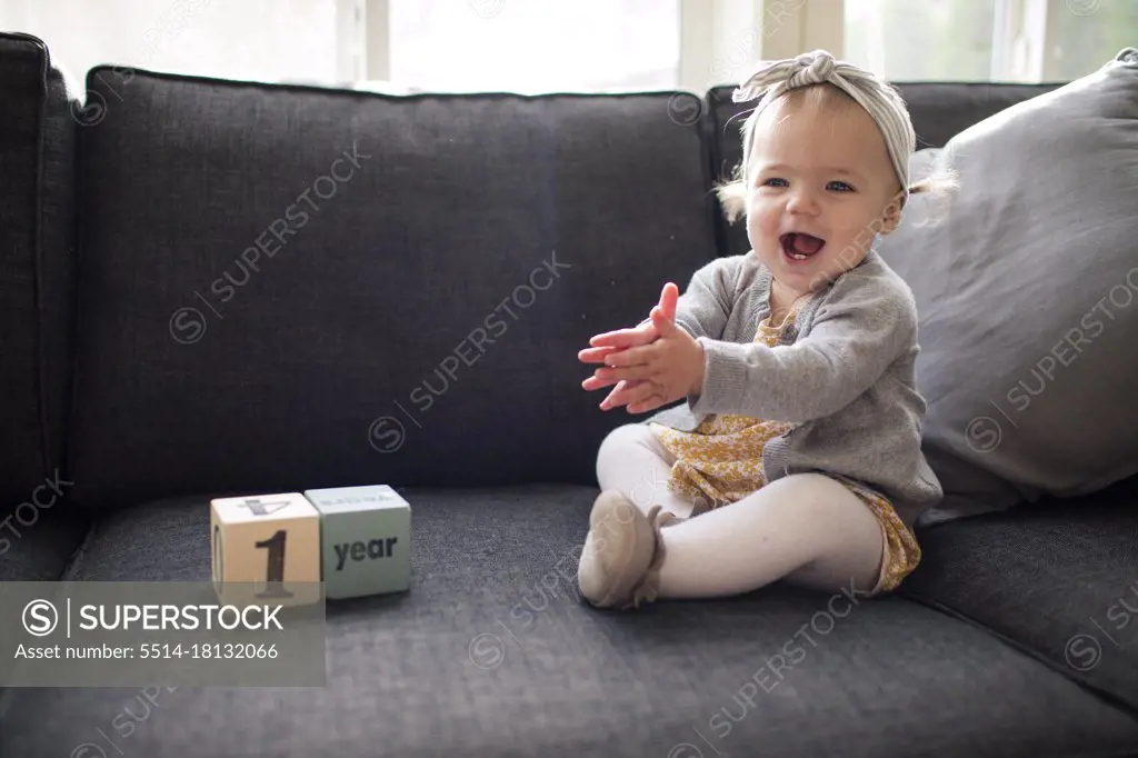 One year old girl sitting on couch clapping with excitement