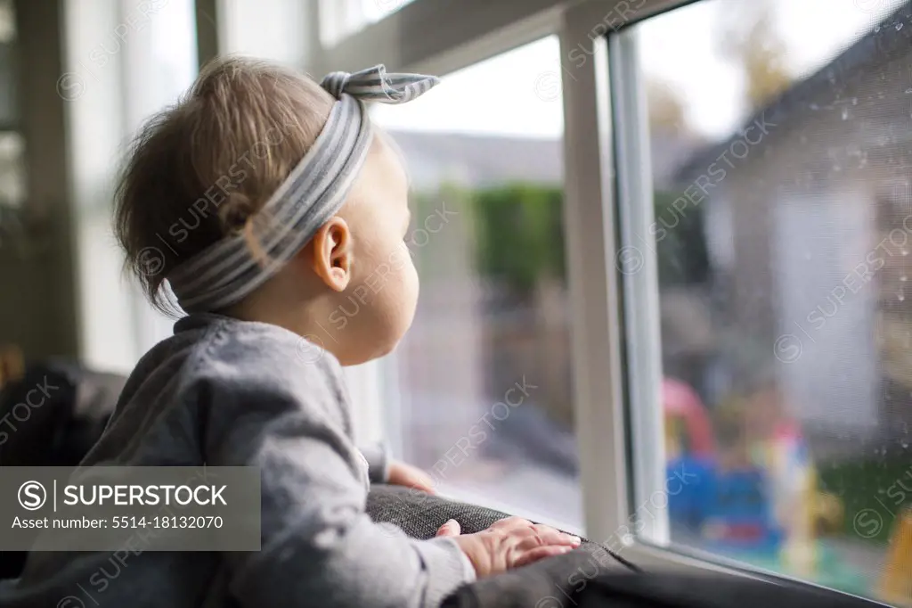 side view of young girl looking out the window into her backyard.