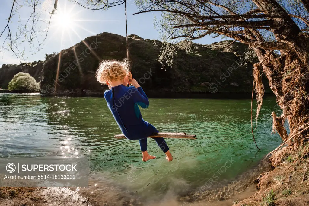 Blonde child on swing over river in New Zealand on sunny day