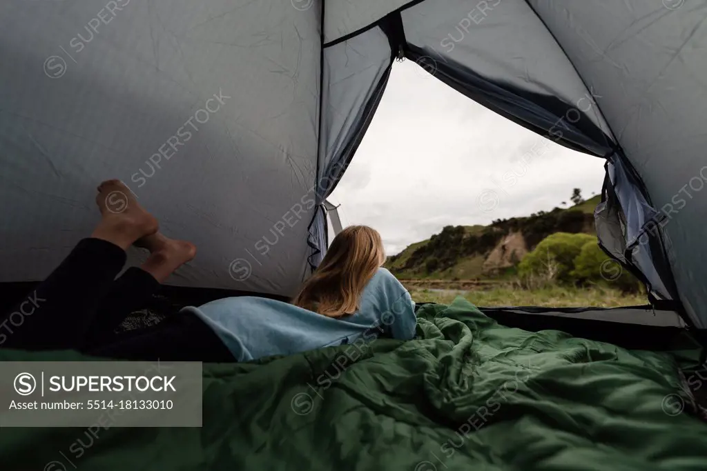 Preteen child lying on sleeping bag in tent on camping trip