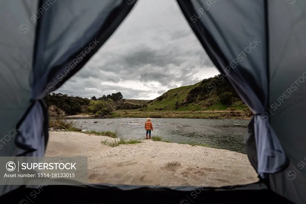 View through tent of child playing near river camping site