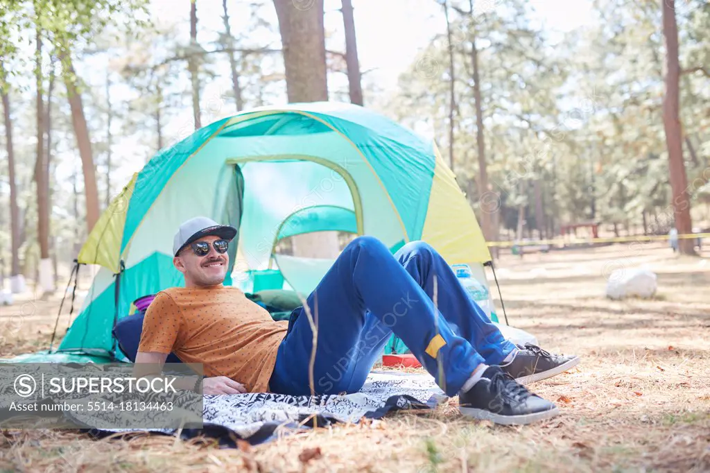 smiling young man with sunglasses lying outside his tent