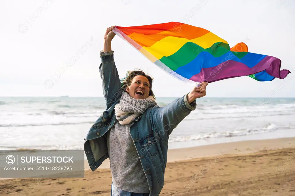Woman running with colorful LGBT flag waving on the beach