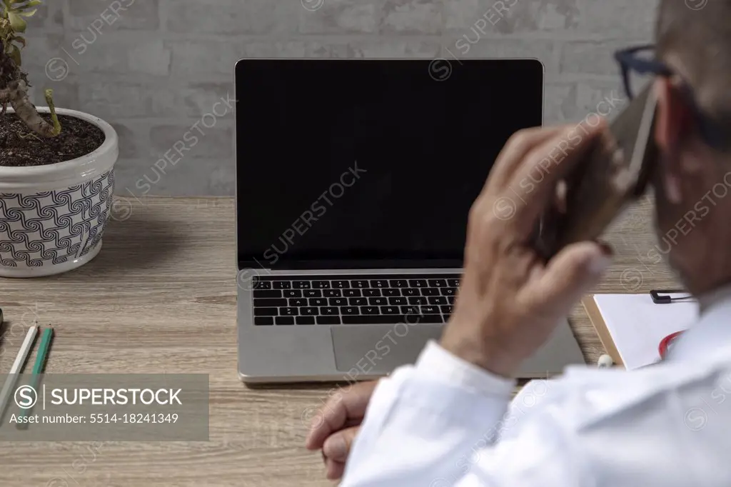 Doctor working with laptop while talking on the phone