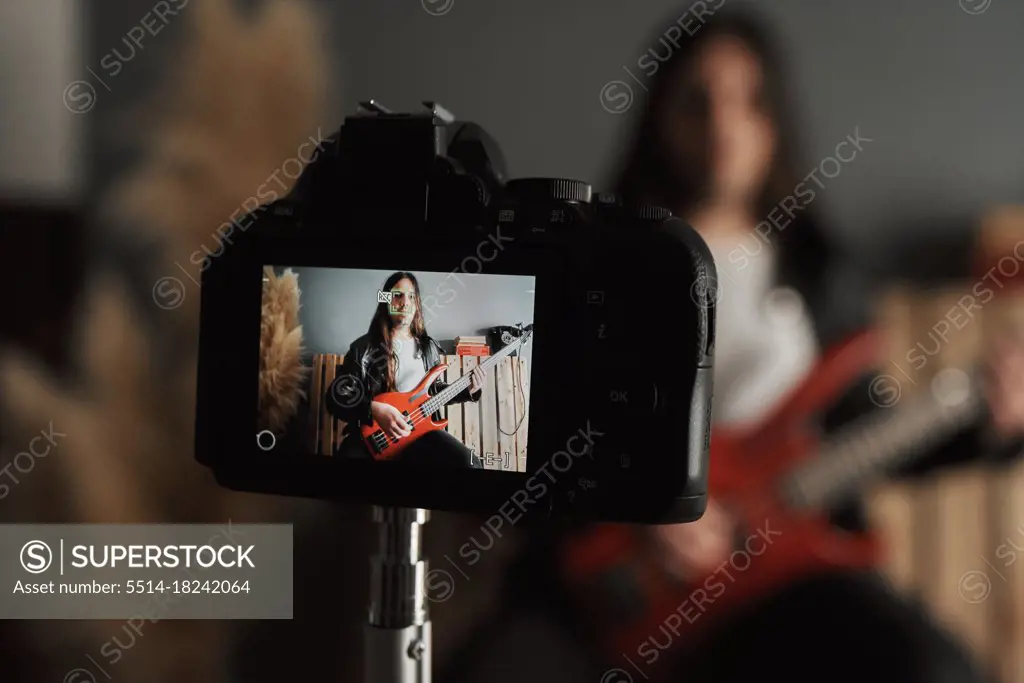 Close-up of a boy filming himself while playing the bass guitar